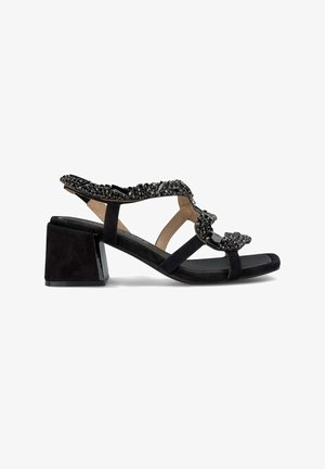 Sandale en suède noir avec un talon bloc, présentant un design supérieur orné de perles et des lanières croisées. Texture lisse avec des accents brillants.