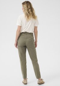 Chino verdi oliva a vita alta con gamba affusolata e una texture liscia. Abbinati a una t-shirt corta di un beige chiaro e scarpe beige.