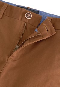 Pantalon en coton marron avec fermeture éclair, bouton en laiton et doublure en denim bleu à l'intérieur de la taille. Présente une texture côtelée et des détails de couture.