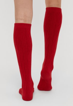 Meias altas até ao joelho, vermelhas, com uma textura canelada e padrão de tricô em cabos. Apresentam um ajuste confortável e um tecido suave. Apropriadas para uso casual.