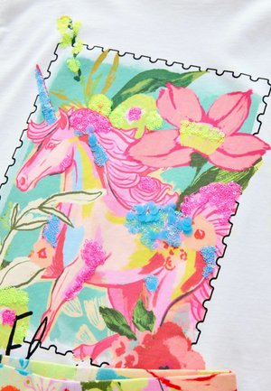 T-shirt blanc avec un design coloré de licorne et de fleurs, rehaussé de sequins rose, vert et bleu, entouré d'une bordure de type timbre.