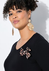 Musta t-paita V-pääntie-muotoilulla, jossa on leopardikuosiset nauha-akcentit. Kultasävyiset korvakorut kerroksellisessa ympyrämuodostelmassa.