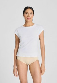 T-shirt bianca a maniche corte con scollatura rotonda e vestibilità rilassata, realizzata in tessuto liscio, abbinata a un sottotono beige chiaro.