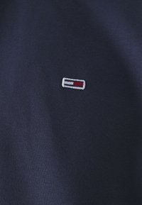 Camiseta de algodón azul marino con un pequeño logo bordado en blanco, rojo y azul en el pecho, con una textura suave y un clásico cuello redondo.