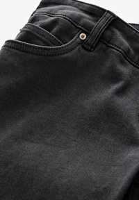 Gros plan sur un jean en denim noir montrant la poche avant, la boucle de ceinture et le détail du rivet métallique sur la texture du tissu.