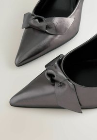 Schwarze Lederpumps mit spitzem Zehenbereich und glänzender Oberfläche, ausgestattet mit einer Schleifenakzent vorne. Glatte Textur und elegantes Design.
