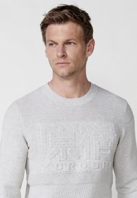 Lichtgrijs gebreid sweater met een gemêleerd patroon en opvallende reliëfletters op de borst. Design met ronde hals.