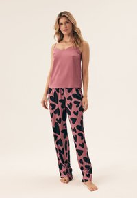 Różowa satynowa koszulka na ramiączkach z cienkimi paskami, połączona z luźnymi spodniami z czarnymi sercami na różowym tle.