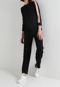 Zwarte sweatshirt met roze logo-stripes op de mouwen, gecombineerd met zwarte joggers en witte sneakers, met een slim fit en elastische boorden.
