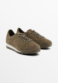 Olive green suede sneakers with textured upper, light gray laces, and a cushioned sole featuring a white stripe. Simple, classic design.