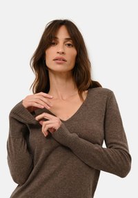 Svetr s výstřihem do V a dlouhými rukávy v tmavě hnědé barvě, s žebrovanými manžetami a měkkým, strukturovaným povrchem. Jednoduchý design s volným střihem.