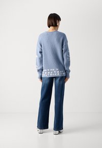 Lys blåstrikket genser med løs passform, som har hvite mønsterdetaljer ved kanten og ermene, kombinert med mørk blå vide jeans.