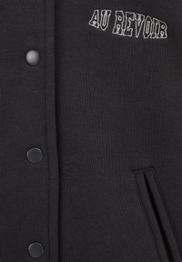 Črna dukserica z strukturiranim dizajnom. Ima v bele barve šivano besedilo "AU REVOIR", zatiče in stranske žepe.