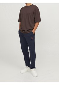 Hnědý bavlněný tričko s volným střihem, spojené s námořnickými tepláky s logem a bílými teniskami. Jednoduchý a ležérní outfit.