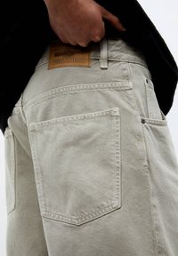Jeans grigi chiaro con una finitura strutturata, dotati di due tasche posteriori, etichetta in pelle marrone e dettagli di cucitura a contrasto.