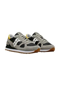 Sneaker grigie e nere con materiali in camoscio e rete, dettaglio bianco, linguetta gialla sul tallone e suola in gomma marrone. Design atletico classico.
