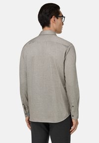 Camicia grigia a maniche lunghe realizzata in tessuto leggero, con colletto a camicia, polsini chiusi con bottoni e orlo curvo.