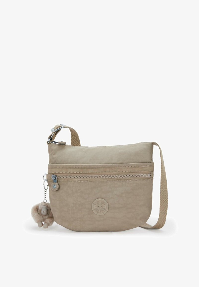 Sac bandoulière beige avec une surface texturée, des compartiments zippés, une sangle ajustable et un bijou décoratif. Logo affiché à l'avant.