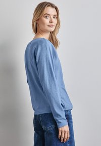 Maglione azzurro chiaro a maniche lunghe con scollatura rotonda e spacchi laterali, realizzato in materiale morbido, abbinato a jeans blu scuro.