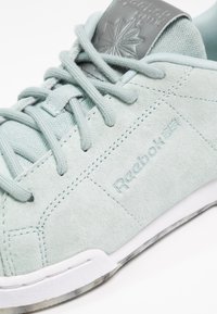 Ljus mintgrön mockasneaker med snörning, strukturerad tunga och vit gummisula. Har präglad logotyp på sidan och hälen.