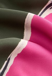 Tissu lisse avec des sections pliées montrant de larges blocs de couleur vert foncé, rose vif et des bords blancs se fondant doucement.