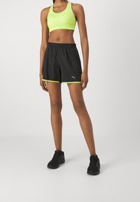 Svarta sportshorts med neongröna detaljer och elastisk midja, tillsammans med en ljusgrön sport-bh med ett triangelmönster.