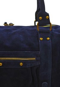 Sac en suède bleu marine avec des accents en métal doré, une poche zippée à l'avant et une bandoulière robuste avec des détails rivetés.