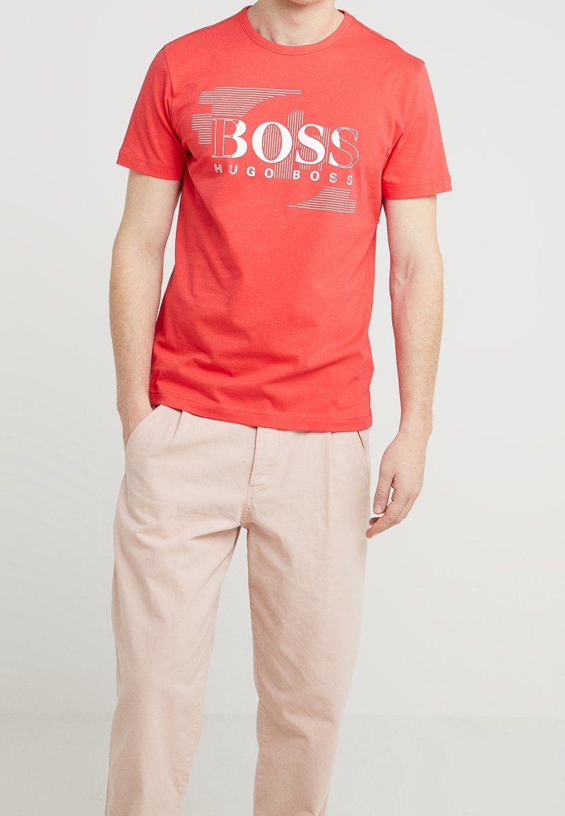 Červené bavlněné tričko s kulatým výstřihem, s bílým grafickým potiskem "BOSS" a "HUGO BOSS" ve výrazných a tenkých liniích.