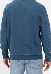 Felpa blu con una finitura morbida e texture e polsini a costine; presenta un logo discreto vicino al collo, abbinata a jeans in denim chiaro.