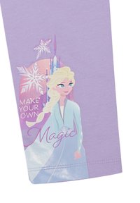 Fioletowa koszulka bawełniana z grafiką postaci z warkoczykami, kryształami i napisem "Stwórz swoją własną magię" w bajkowym kroju pisma.