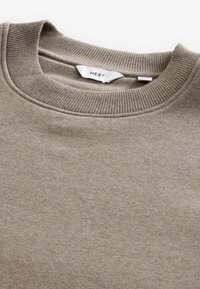 Sudadera color beige con cuello redondo acanalado y textura suave. La etiqueta dice "NEXT", con un diseño simple y limpio.