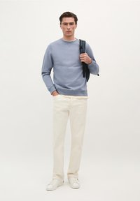 Lichtblauwe sweater, crèmekleurige broek en witte sneakers. De sweater heeft een geribde halslijn en manchetten, terwijl de broek een gladde textuur heeft.