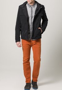 Czarna kurtka na zamek i guziki, szara koszula, pomarańczowe spodnie oraz szare buty z niebieskimi podeszwami, stojące na neutralnym tle.