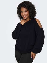 Pull noir en maille avec découpes aux épaules, manches larges et coupe décontractée. Le modèle le porte avec des leggings noirs.