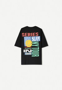 Black oversized t-shirt featuring multicolored graphic prints, including "SERIES," "SLAM," and a yellow tennis ball. Soft cotton material.