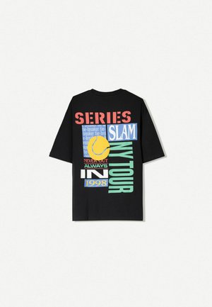T-shirt noir surdimensionné avec des impressions graphiques multicolores, y compris "SERIES", "SLAM" et une balle de tennis jaune. Matériau en coton doux.