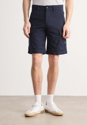 Navy cargo shorts laget av bomull med en avslappet passform, med sidelommer og brettet kant. Kombinert med hvite sneakers og ankelsokker.