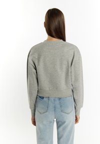 Grijs cropped sweatshirt met een ronde halslijn en geribbelde zoom, gecombineerd met lichtblauwe high-waisted jeans met versleten details.