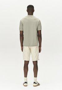 Ljusgrön kortärmad stickad polotröja, beige rullade shorts, vita strumpor med mörka detaljer och svartvita sneakers.