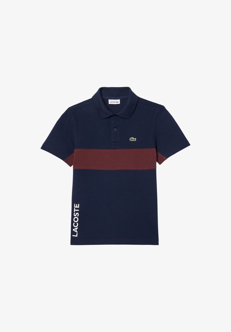 Polo bleu marine avec une bande horizontale bordeaux, logo Lacoste sur la poitrine et texte « LACOSTE » vertical sur le bas côté gauche.