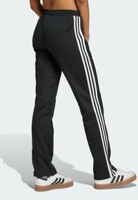 Černé sportovní kalhoty s bílým třemi pruhy po stranách, vybavené elastickým pasem a hladkým povrchem.