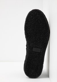 Suola di scarpa in gomma nera con una superficie testurizzata e decorata. Presenta un piccolo etichetta del marchio incorporata sul lato della suola.