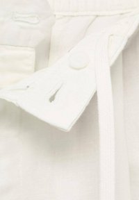 Gros plan sur un tissu blanc présentant un bouton, des coutures renforcées et une boucle au col. Texture douce avec une finition légèrement brillante.