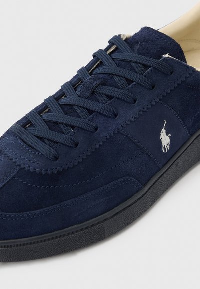 Ναυτικό μπλε σουέτ αθλητικό παπούτσι με υφασμένη επάνω επιφάνεια, επίπεδα κορδόνια και λευκή λογότυπη λεπτομέρεια. Διαθέτει ενισχυμένα ραφές και καουτσούκ σόλα.