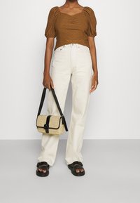 Brun strukturerad topp med puffärmar, högmidjade vita jeans och svarta remsandaler. Håller en beige väska med svart rem och spänne.