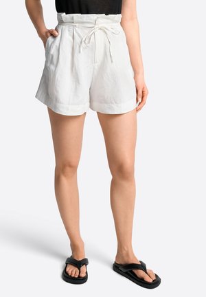 Weiße Leinen-Shorts mit hohem Bund, Bindegürtel und hochgekrempeltem Saum. Kombiniert mit schwarzen Flip-Flops, die einen lässigen Sommerlook zeigen.