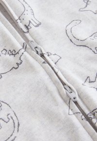 Grenouillère zippée en coton gris clair ornée d'un motif de dinosaure en gris foncé. Fermeture à glissière blanche. Tissu doux et texturé.