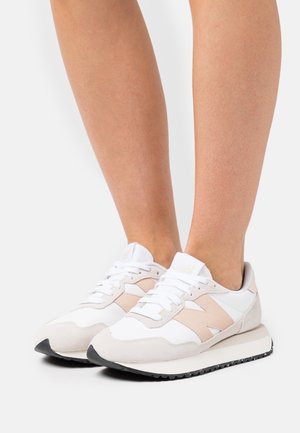 Sneakers charakteryzują się połączeniem białej skóry i beżowego zamszu z czarną gumową podeszwą. Zaokrąglony czubek i klasyczny system sznurowania.