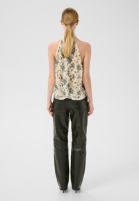 Top halter bej fără mâneci, cu un model floral și paiete, asortat cu pantaloni din piele verde închis. Textură netedă, design care se mulează pe corp.