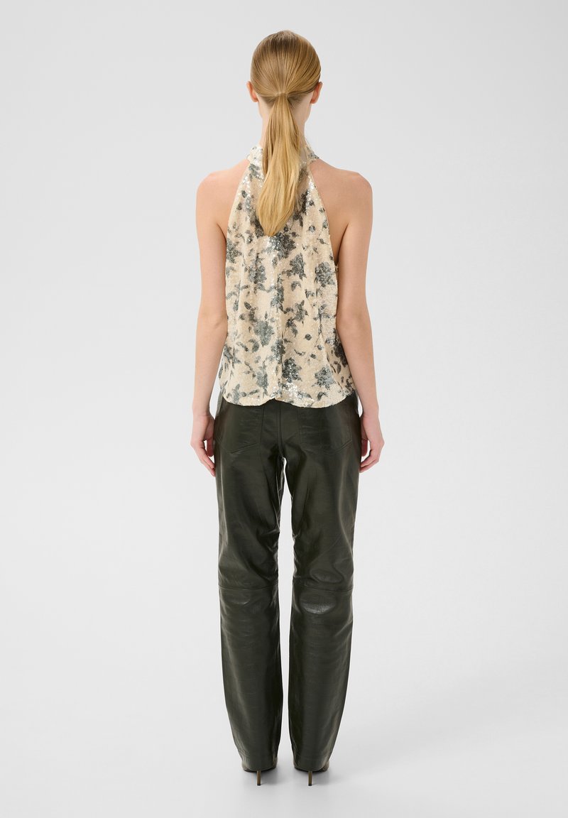 Ärmeloses beige halterneck-top med blomstermønster og paljetter, parret med mørkegrønne læderbukser. Glat tekstur, tætsiddende design.